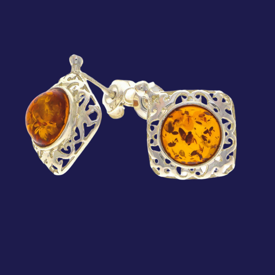 Each piece showcases a captivating Nordic natural amber cabochon in a warm honey or cognac hue, harmoniously set within an intricately filigreed bezel featuring swirling scrollwork motifs.