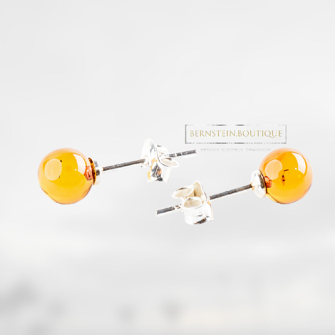 Shiny, partially transparent stud earrings with honey-gold to orange peel amber beads